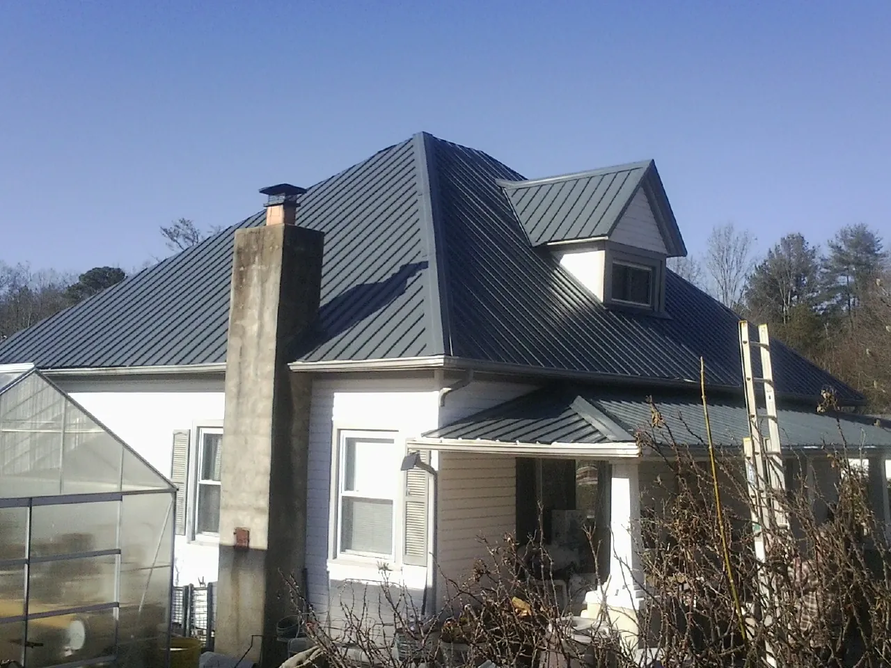 Dark blue standing seam metal roof on a white farmhouse with dormer — Slate & Tile Roof Repair by Roofing Brothers in Romayor