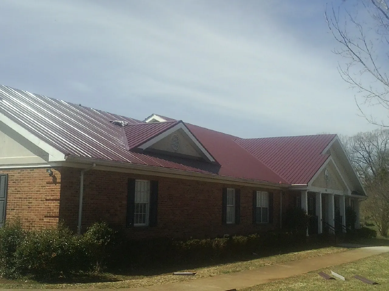 Red metal roof with gabled entries on a long brick building, from a Hail Damage Roof Repair job in Romayor