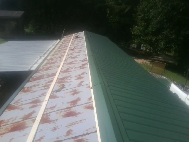 Old rusted panels beside newly installed green metal roofing — Wind Damage Roof Repair by Roofing Brothers in Romayor