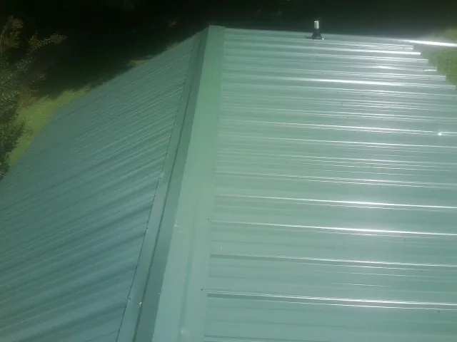 New green metal panels meeting at the ridge of a roof — Flat Roof Repair work by our crew in Romayor