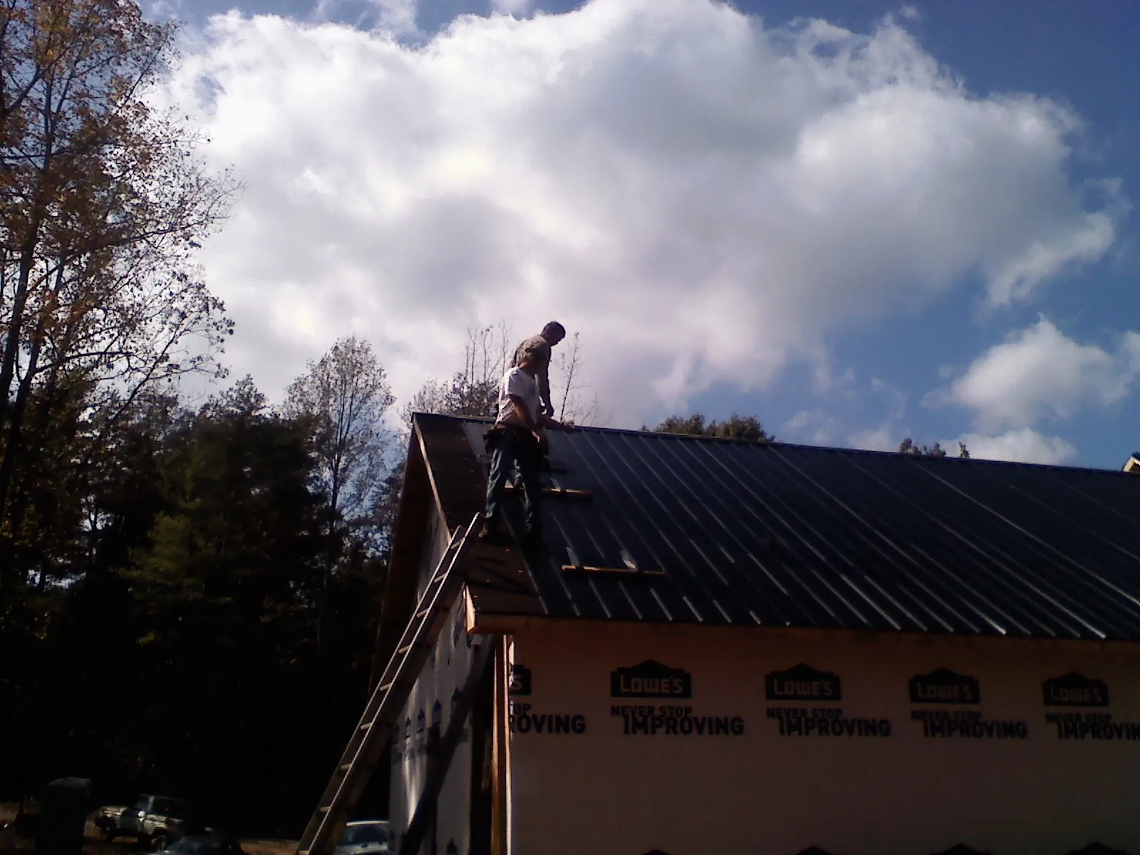 Roofer fastening dark metal panels high against a cloudy sky, from a Roof Inspection job in Romayor