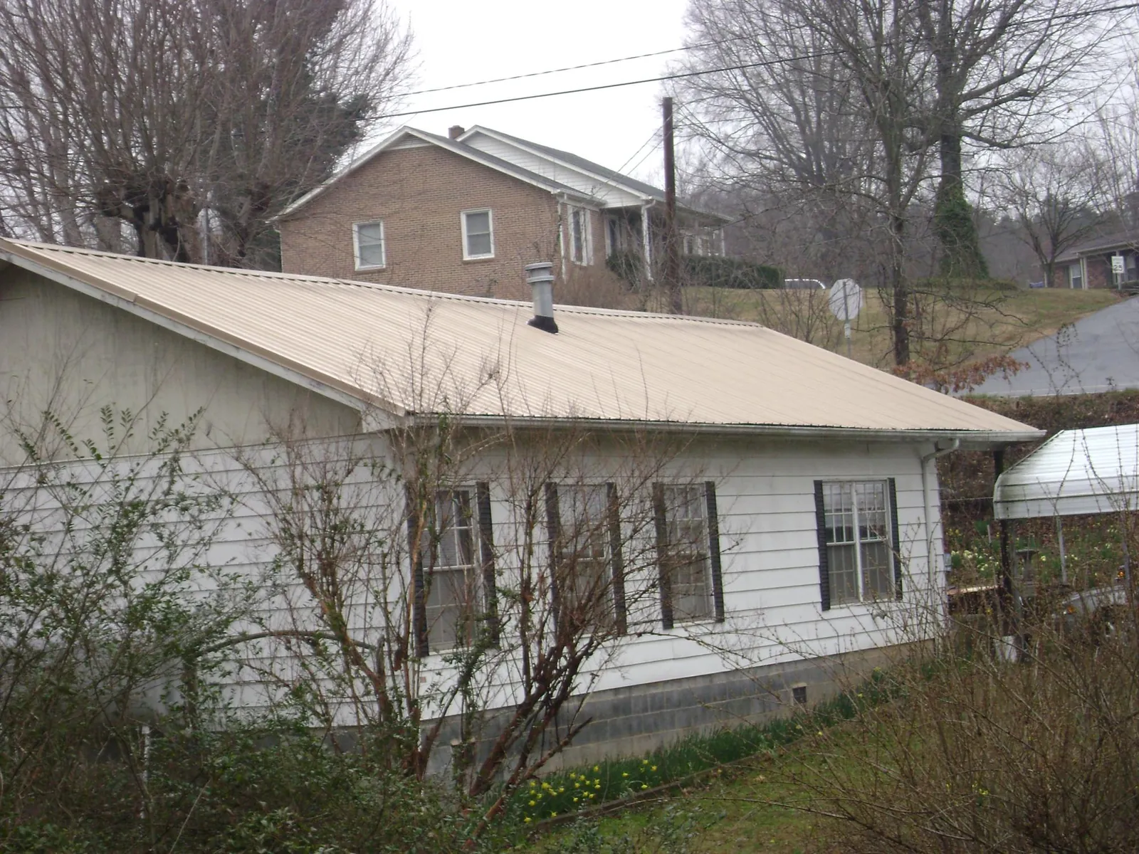 Tan metal roof on a white sided house set into a hillside — Commercial Roofing by Roofing Brothers in Romayor