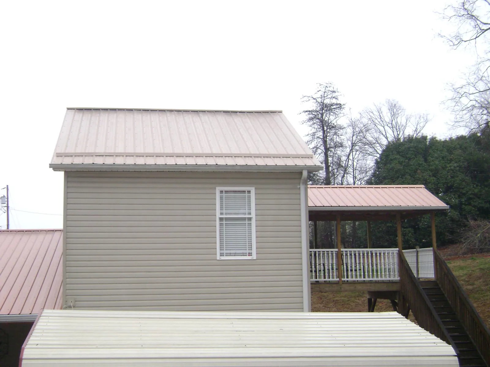 Tan metal roofs on a two story addition and attached porch, from a Roof Replacement job in Romayor